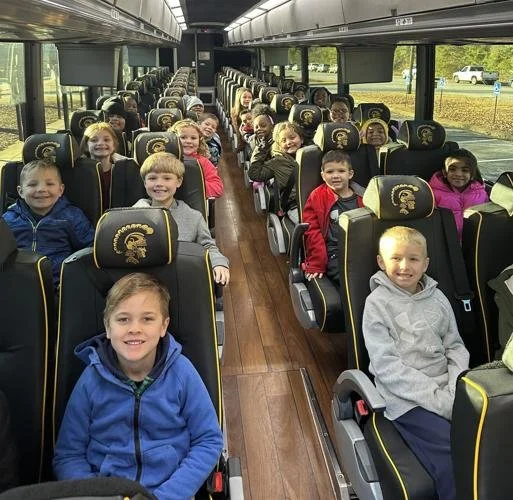 Children sitting on a school bus with black and yellow seats, smiling at the camera.
