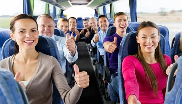 Happy group of people sitting on a bus, giving thumbs up and smiling.
