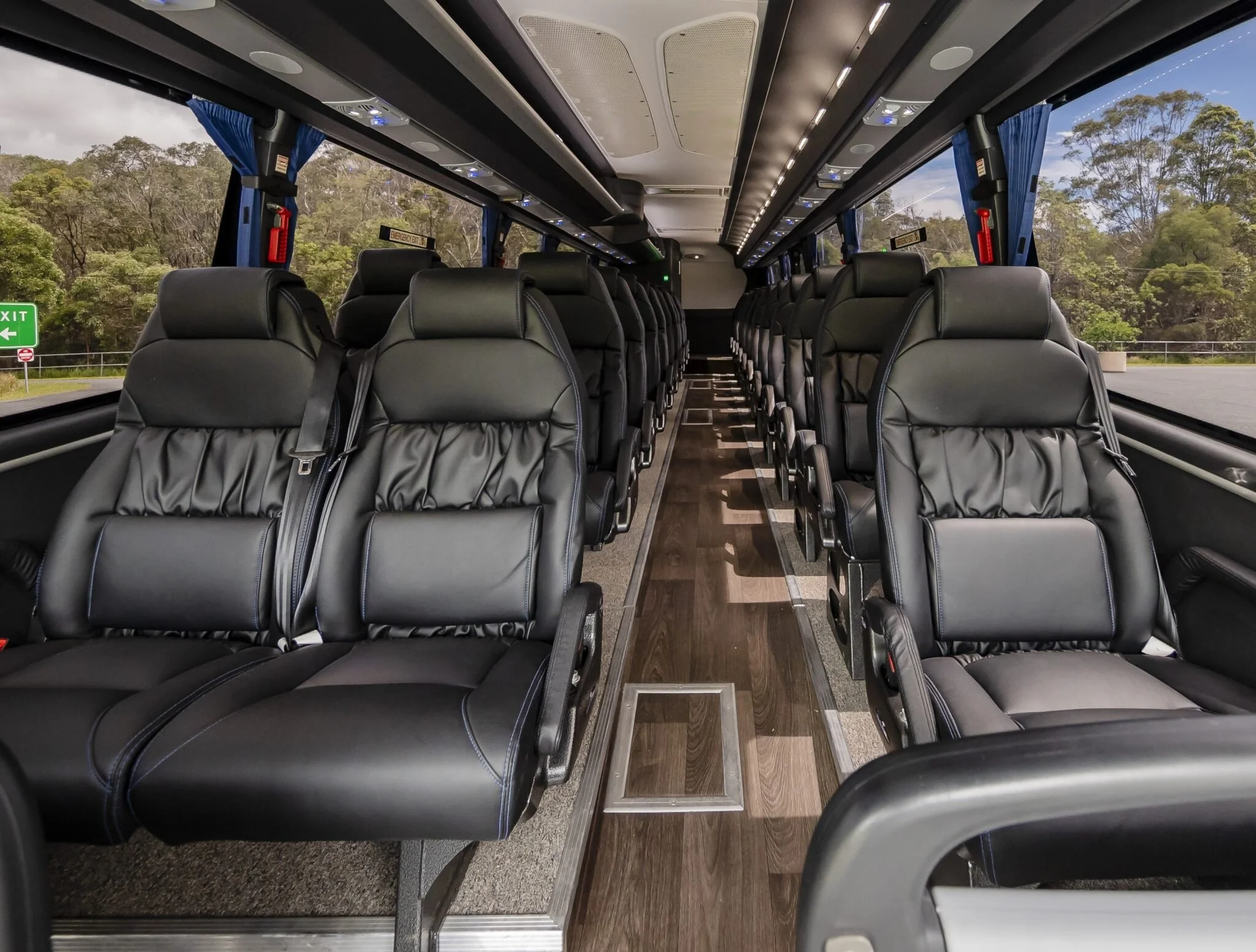 Interior of a modern bus with black leather seats, wood flooring, and large windows showing a green landscape outside.