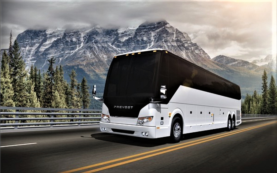 A white and black modern tour bus driving on a highway through a mountainous forested area.