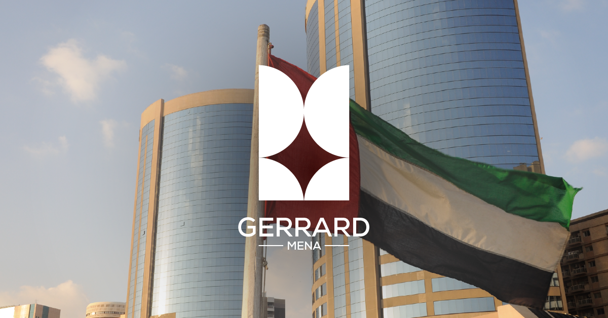 A flag with horizontal stripes of red, white, green, and black flying in front of tall, modern glass skyscrapers.