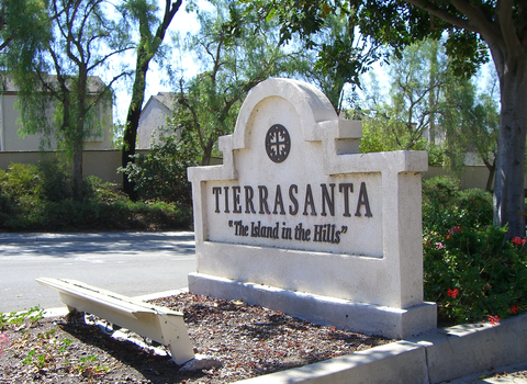Stone sign reading 'TIERRASANTA The Island in the Hills' in a landscaped area, with trees and a bench nearby.