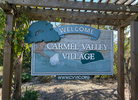 Welcome sign for Carmel Valley Village with a tree and rocks illustration.