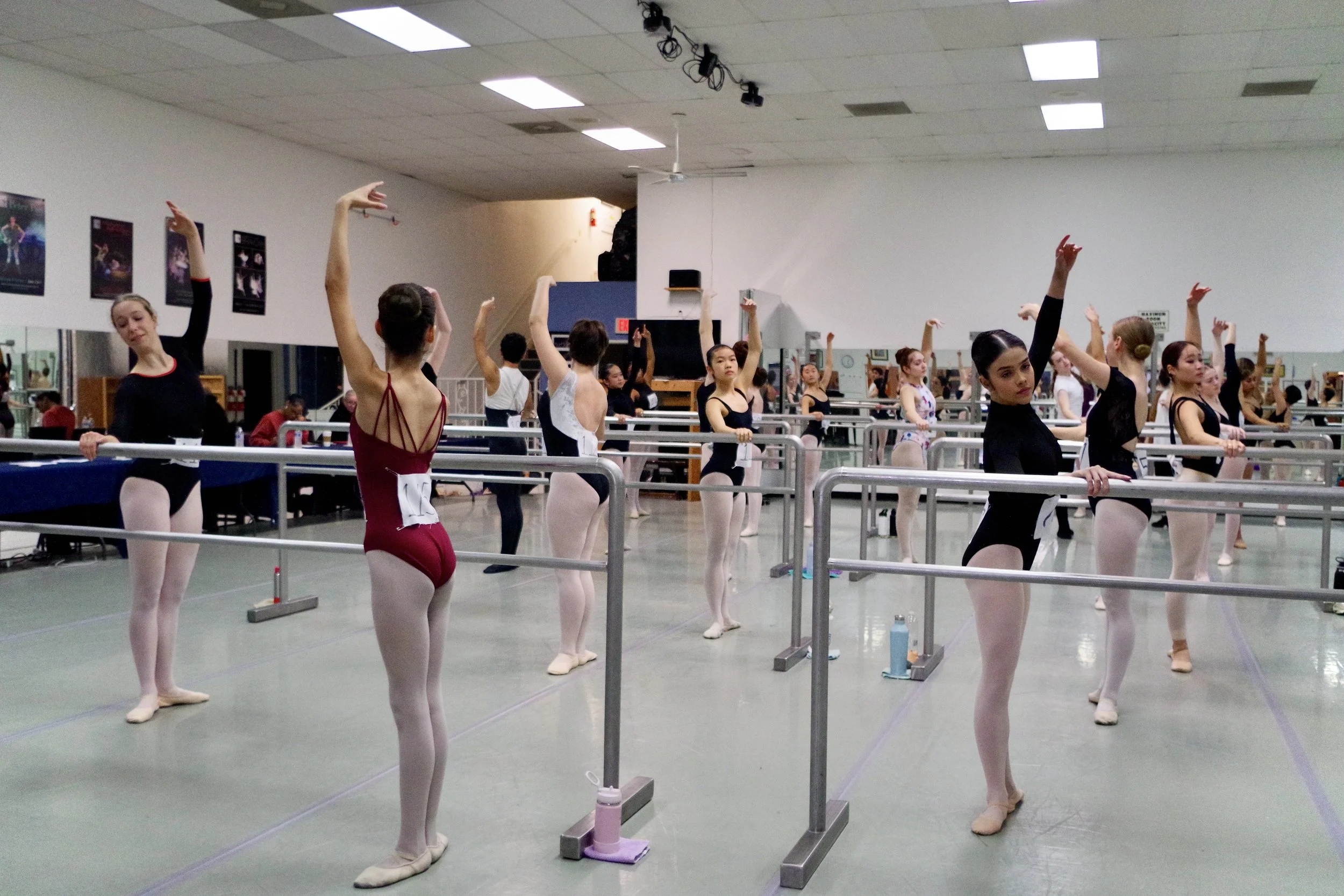 Ballet dancers practicing at a dance studio with mirrors, ballet barre, and posters on the wall.