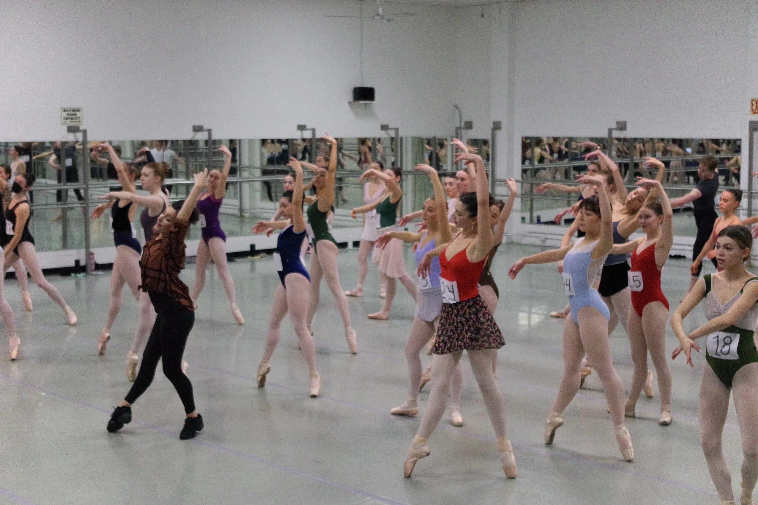 Ballet students practicing in a dance studio with mirrors and ballet barres.