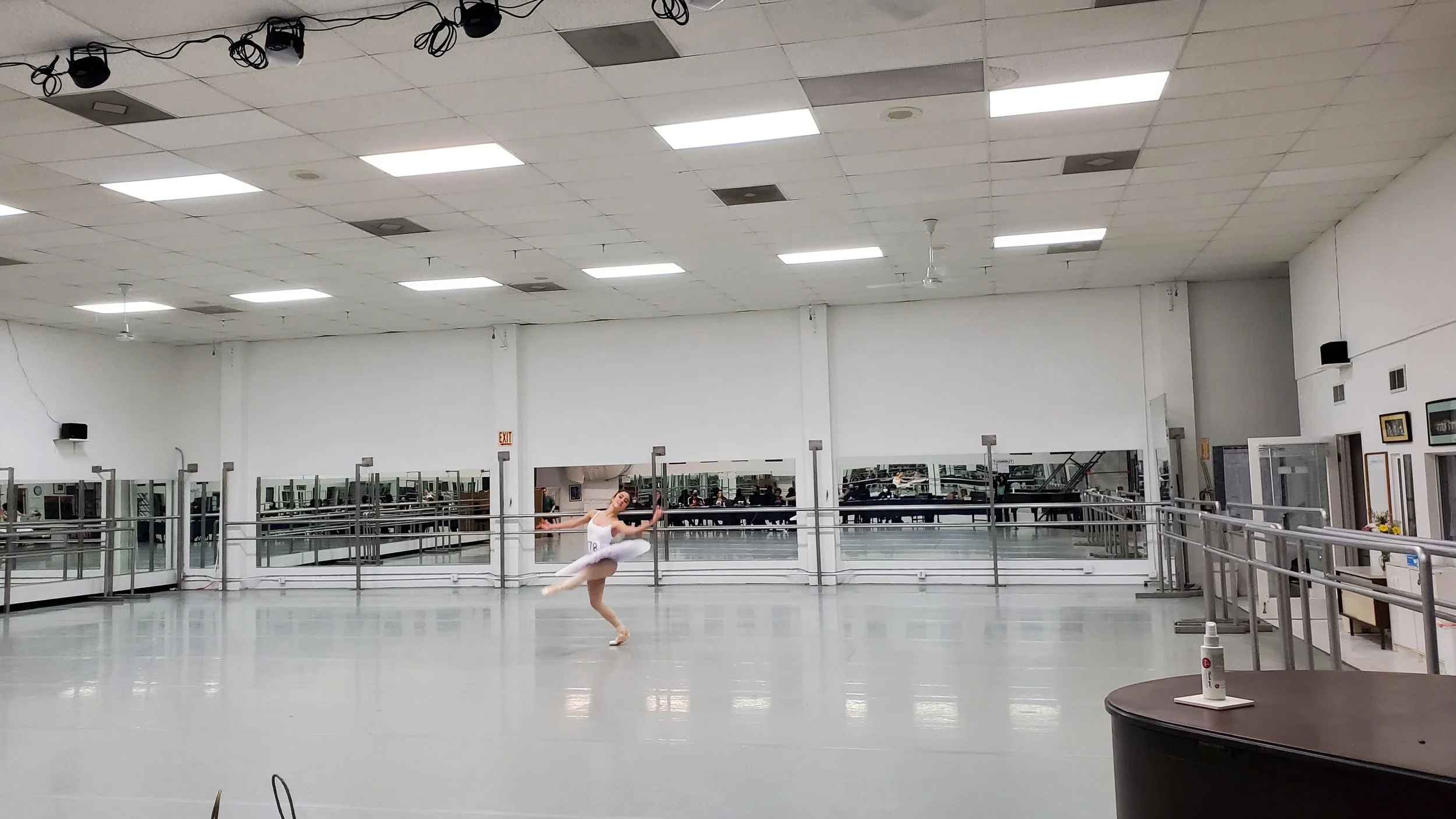 A ballet dancer practicing alone in a spacious dance studio with mirrored walls and ballet barres.