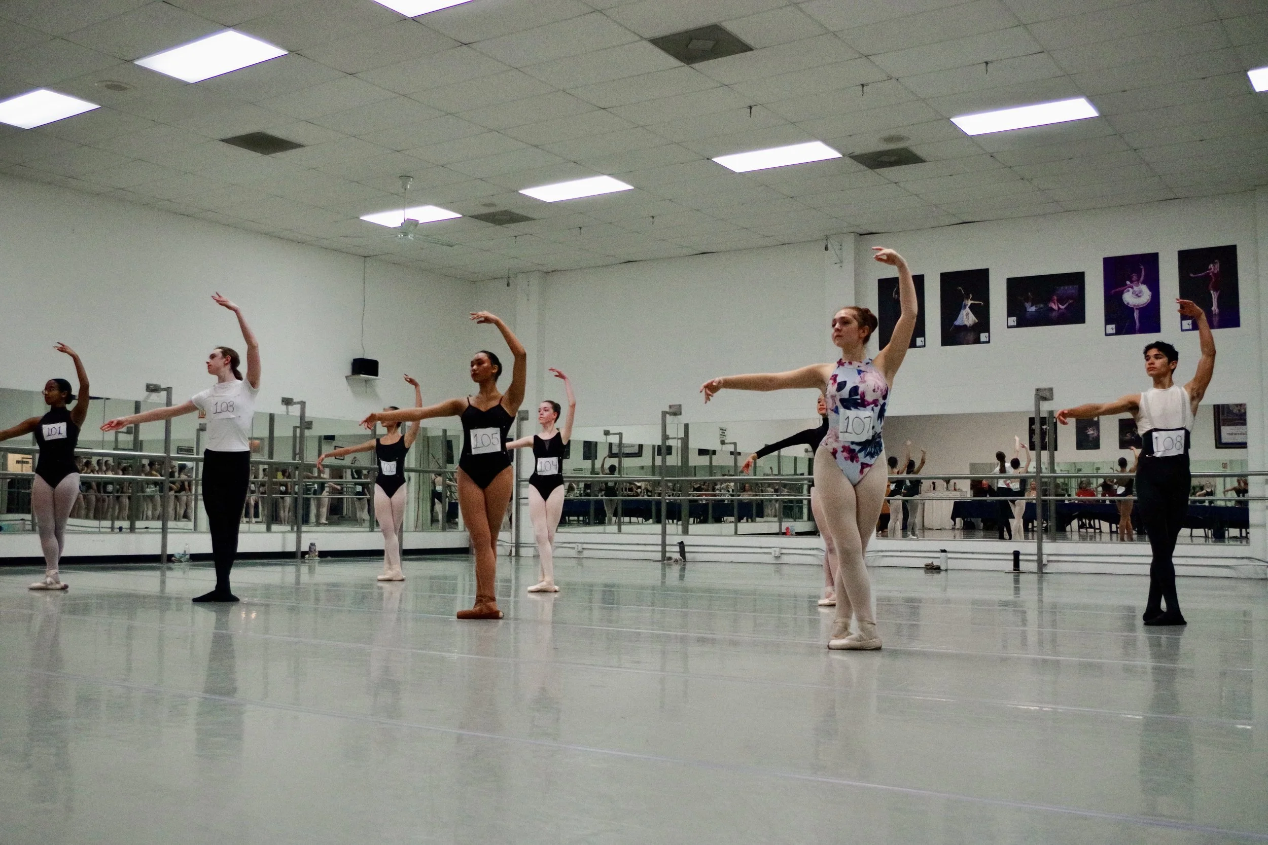 Ballet dancers practicing in a dance studio with mirrors and framed pictures on the wall.