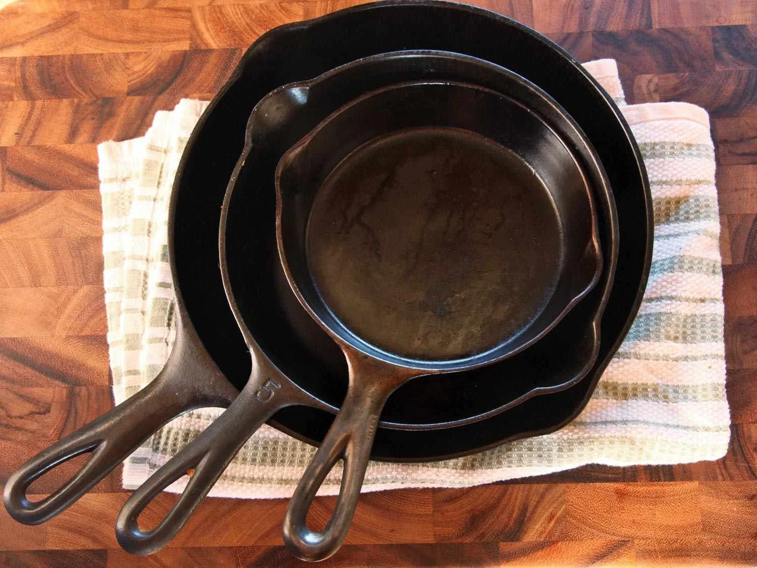 Stack of three cast iron skillets of varying sizes on a striped kitchen towel on a wooden countertop.