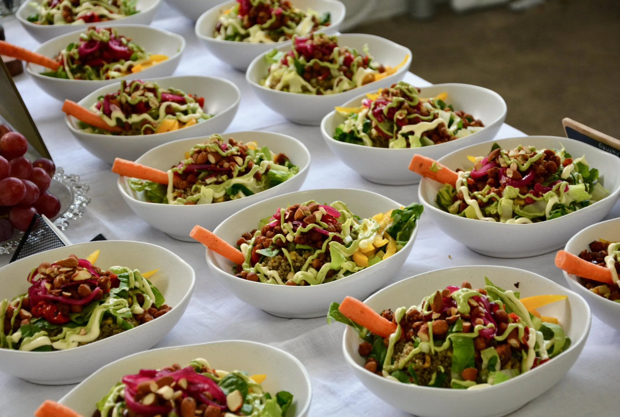 Multiple bowls of salad with lettuce, carrots, shredded cheese, and toppings on a white tablecloth.