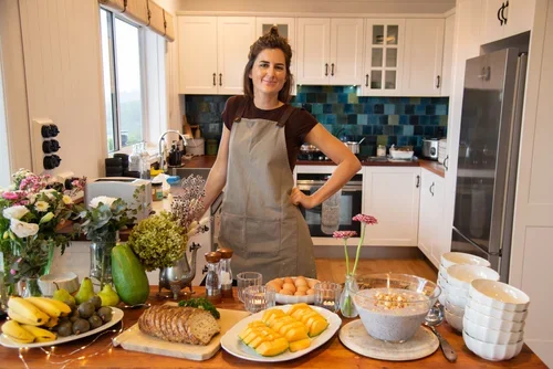 Woman standing in kitchen with various ingredients and dishes on counter, smiling