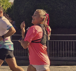 Woman running outdoors in a pink shirt, with a backpack, near a railing and trees.