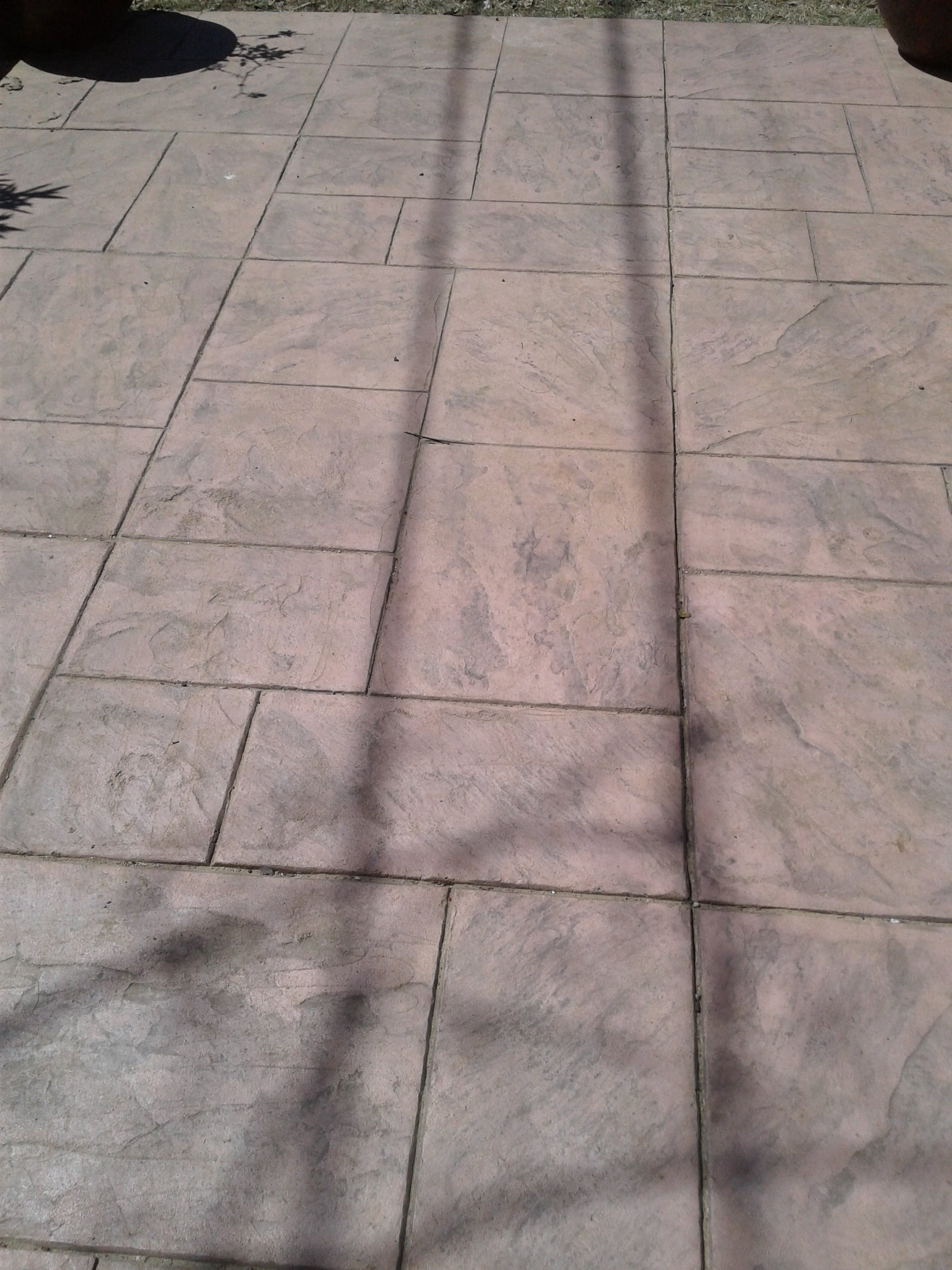 Concrete sidewalk with rectangular paving stones and shadows cast from nearby objects.