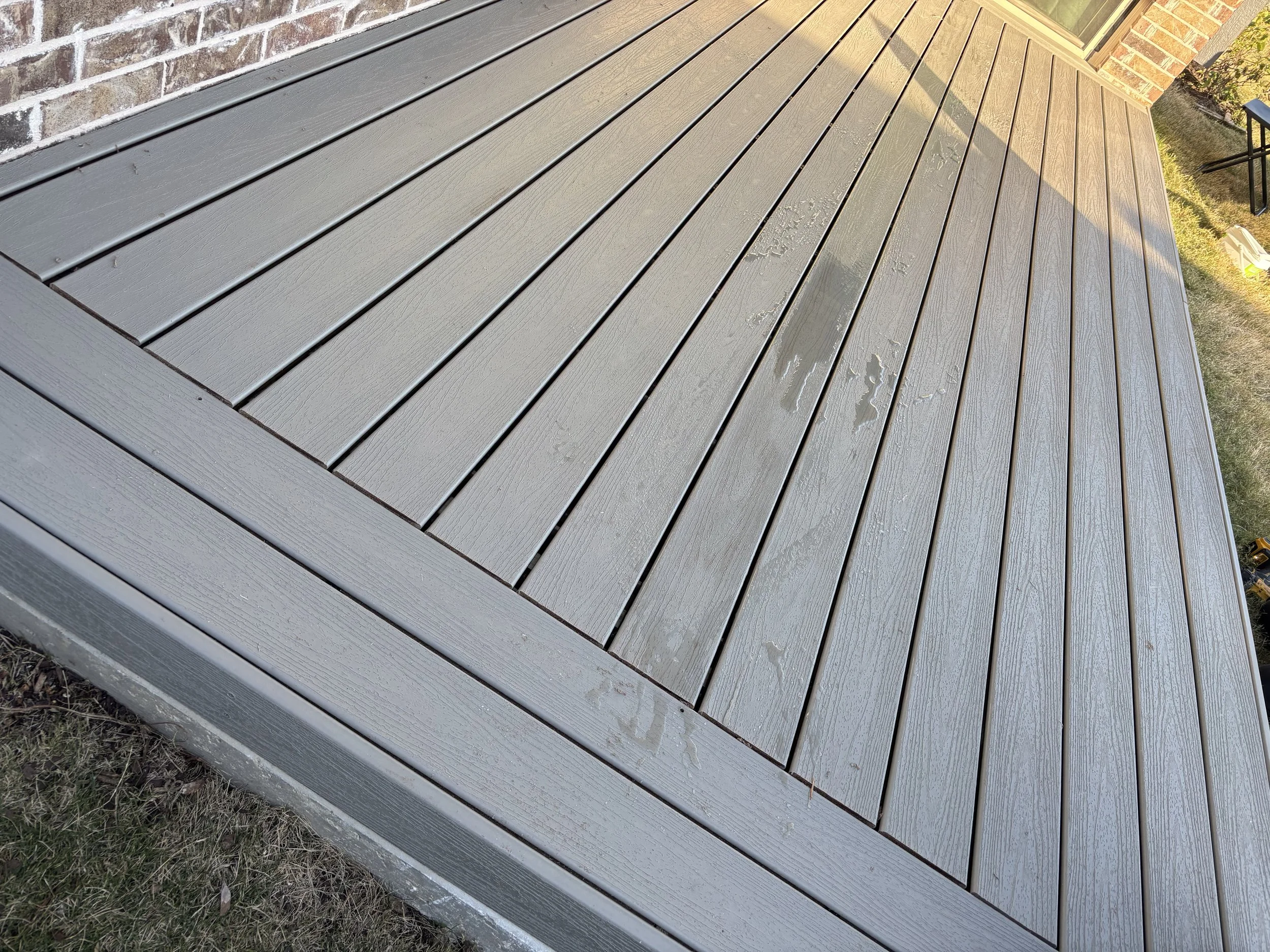Close-up view of a newly painted gray wooden deck outside a house, with some water spots on the surface.