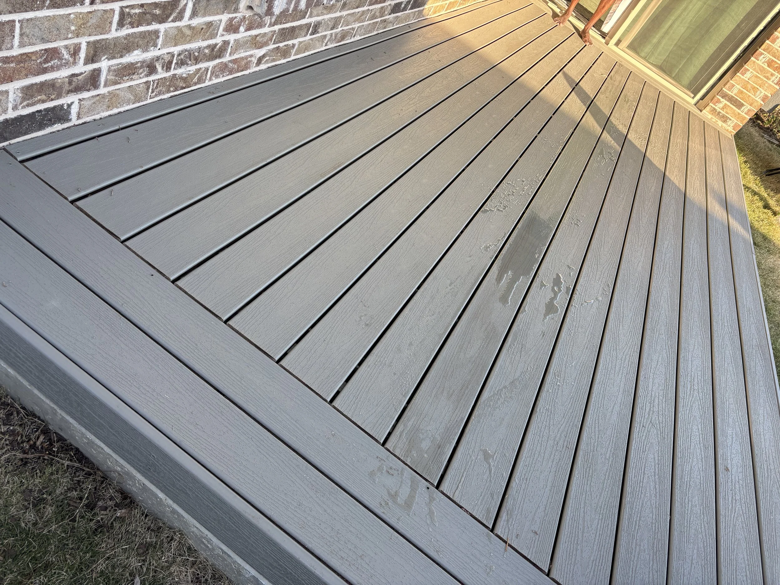 A newly painted gray wooden deck outside a brick house with a sliding glass door.