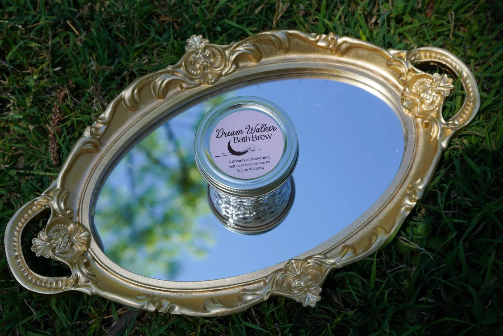 Dream Walker bath brew jar placed on a vintage gold mirror tray outdoors on grass.