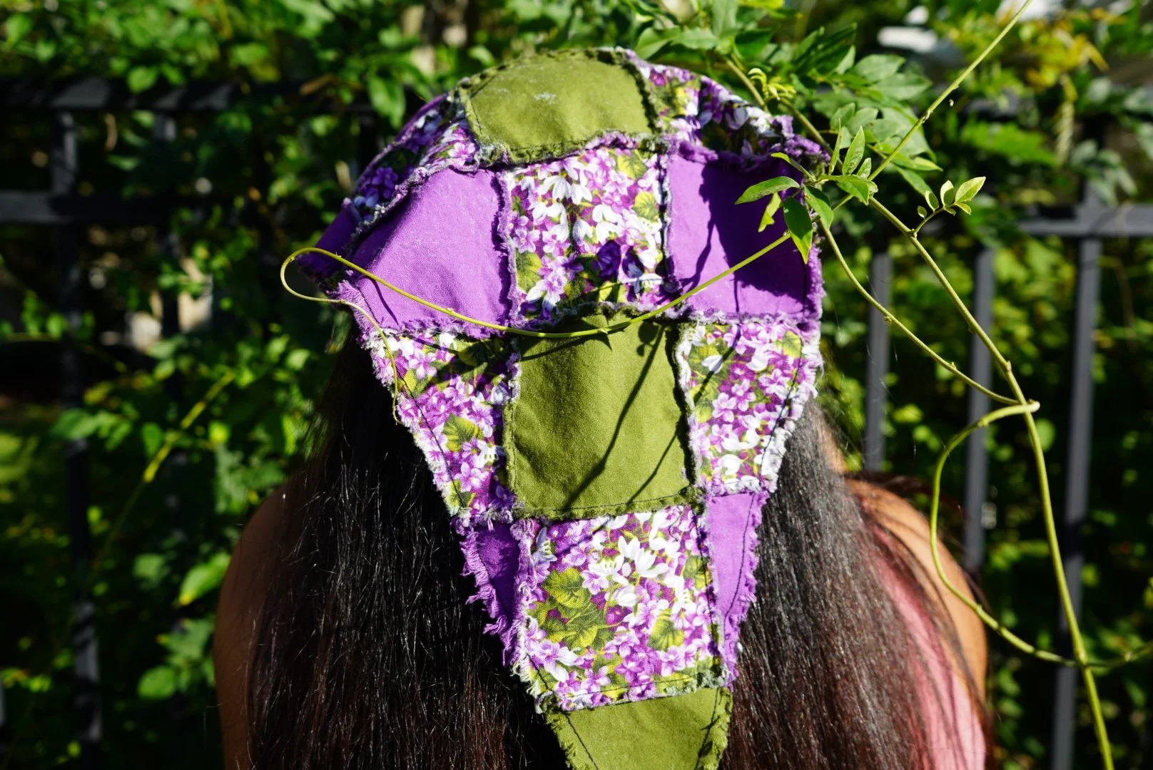 Fringe quilt style patchwork veil in purple and green floral fabrics worn outdoors among green vines in sunlight.