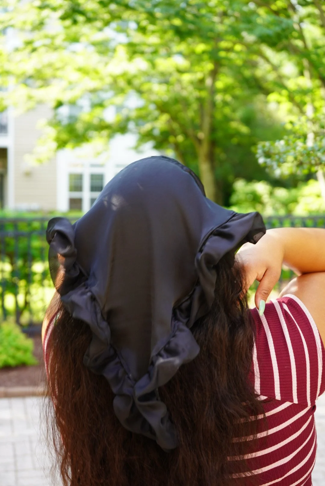 Black satin veil with ruffled edges worn outdoors in sunlight with greenery in the background.