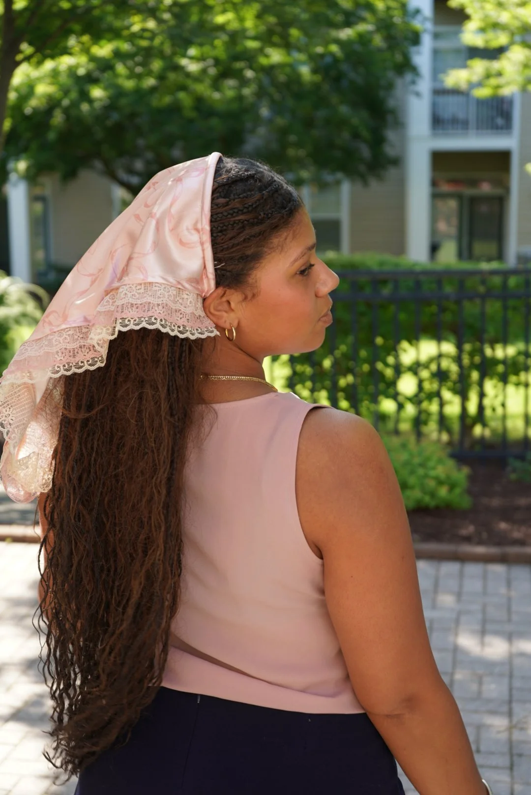 Light pink satin veil with lace trim worn outdoors in sunlight with greenery in the background.