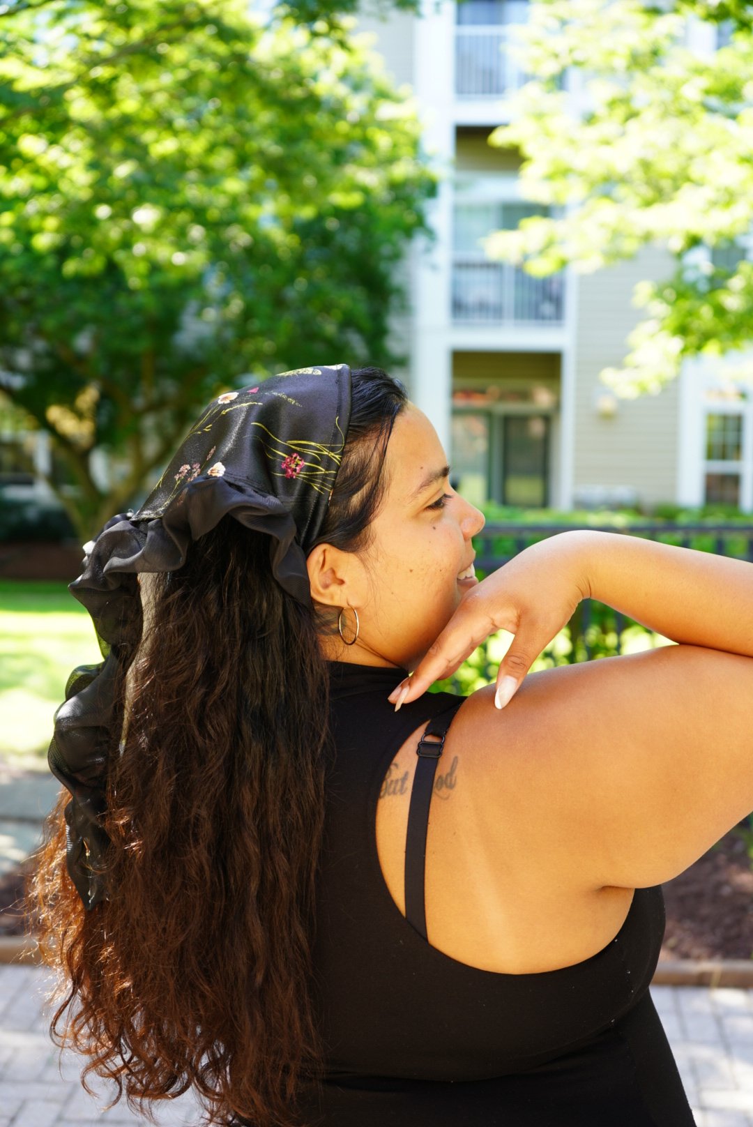 Black floral-patterned veil with ruffled edges worn outdoors in sunlight with greenery in the background.