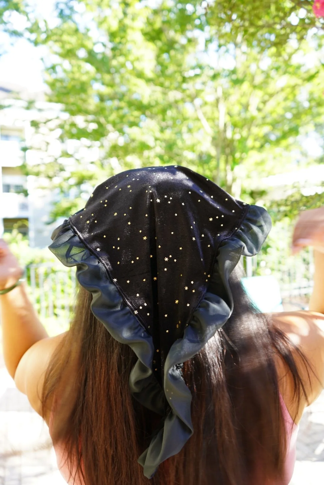 Black star-patterned veil with ruffled edges worn outdoors in sunlight with green trees in background.