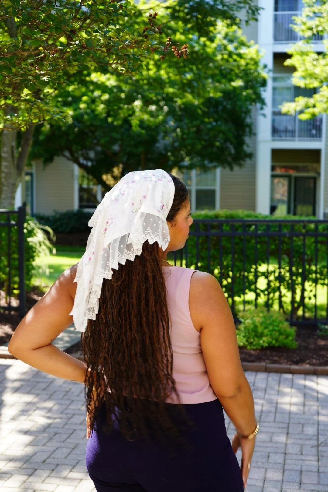 White floral veil with lace trim worn outdoors in sunlight with greenery in the background.
