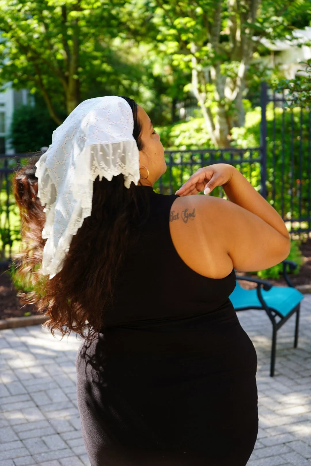 White and blue lace veil with embroidered detail worn outdoors in sunlight with greenery in the background.