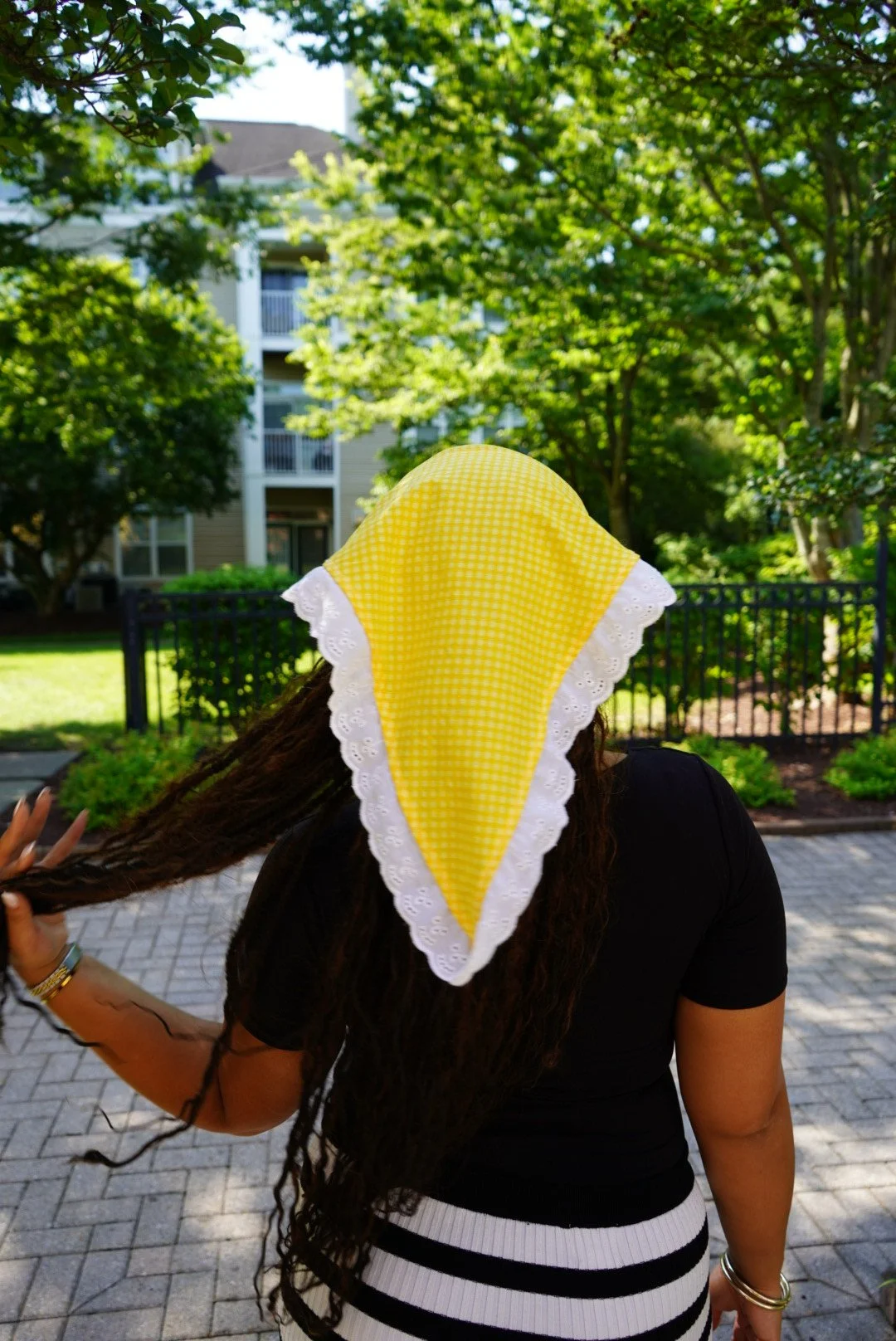 Yellow gingham veil with white lace trim worn outdoors in sunlight with greenery in the background.