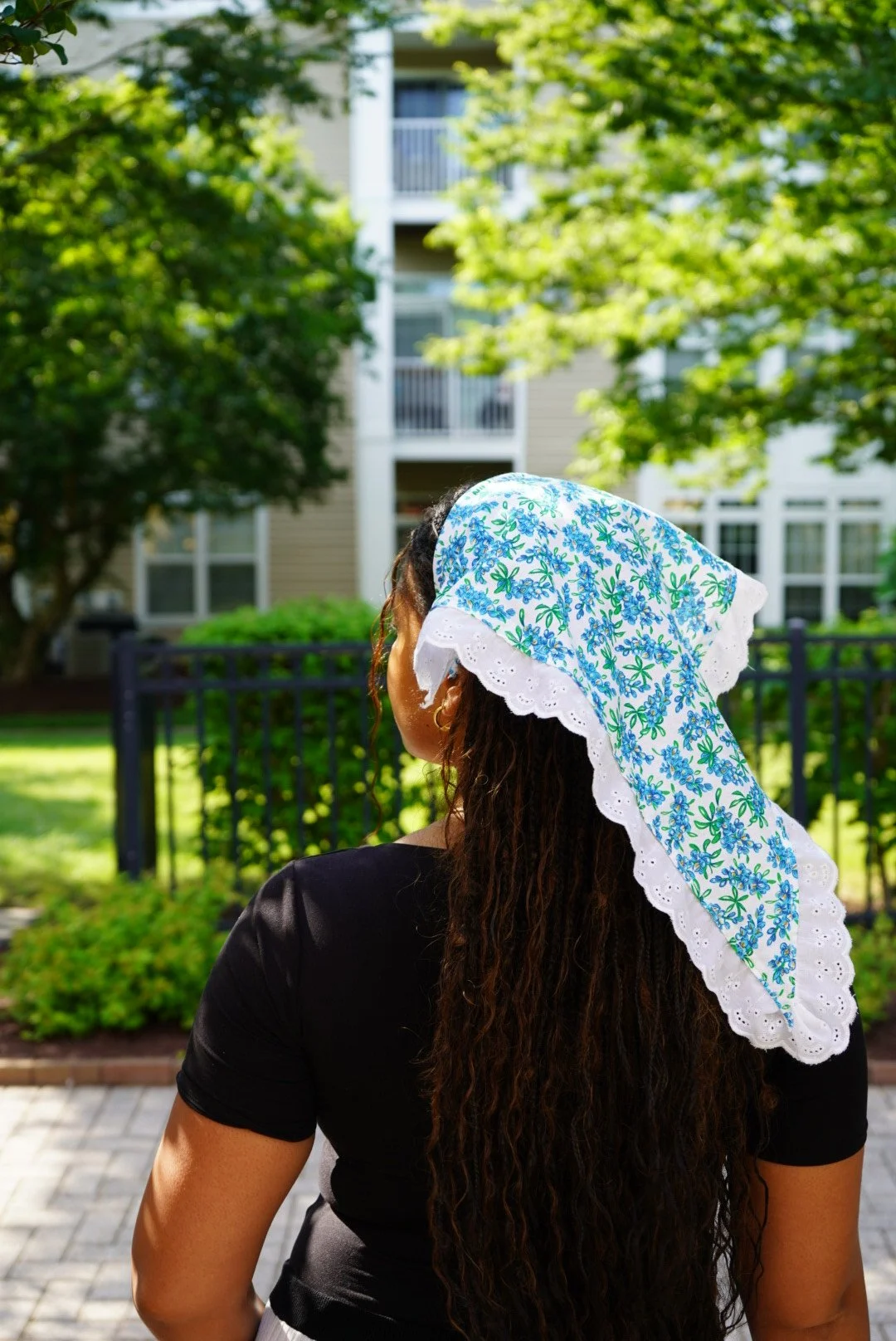 White veil with blue floral pattern and lace trim worn outdoors in sunlight with greenery in the background.