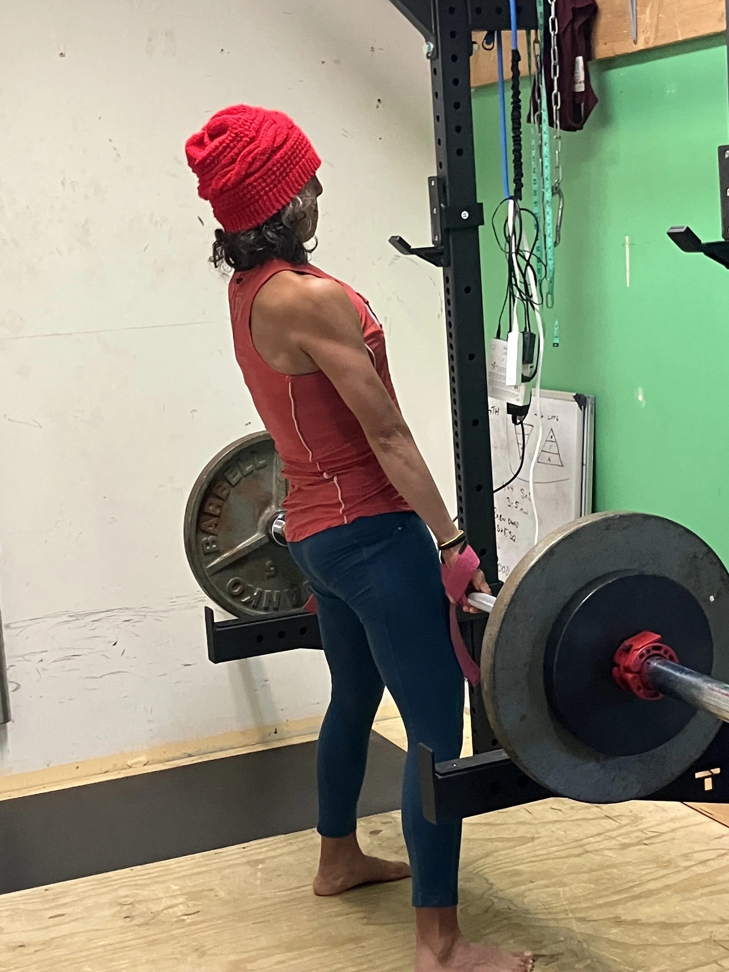 A woman with a red knit hat and a red tank top lifting a barbell in a gym.