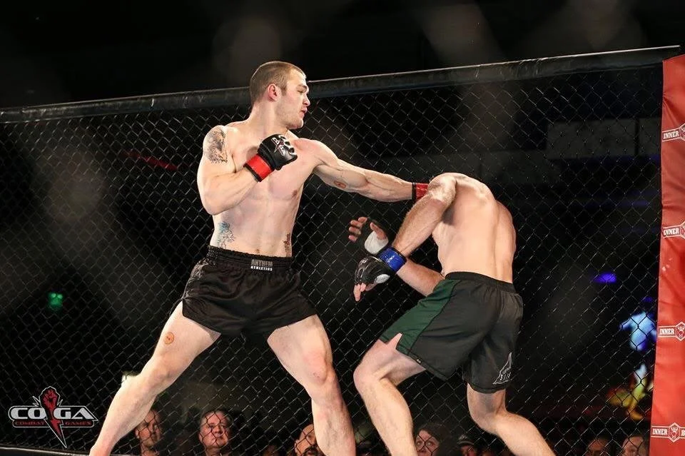 Two mixed martial arts fighters are engaged in a fight inside a cage, with one delivering a punch to the other's head.