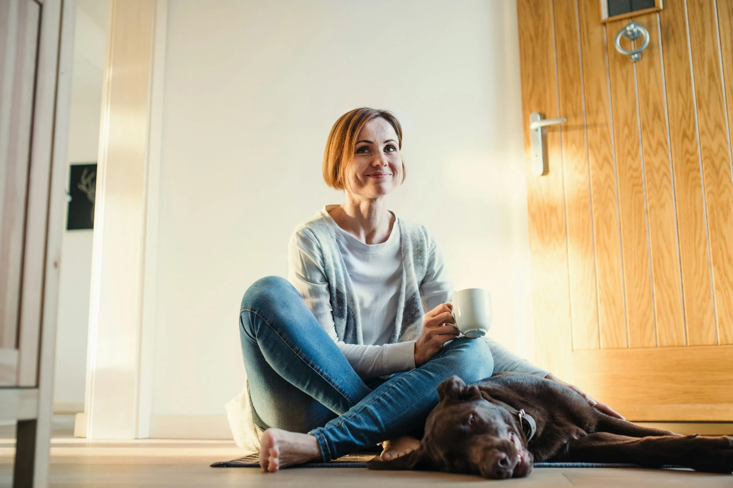 a woman sitting happily on the floor with her calm dog after training sipping her coffee