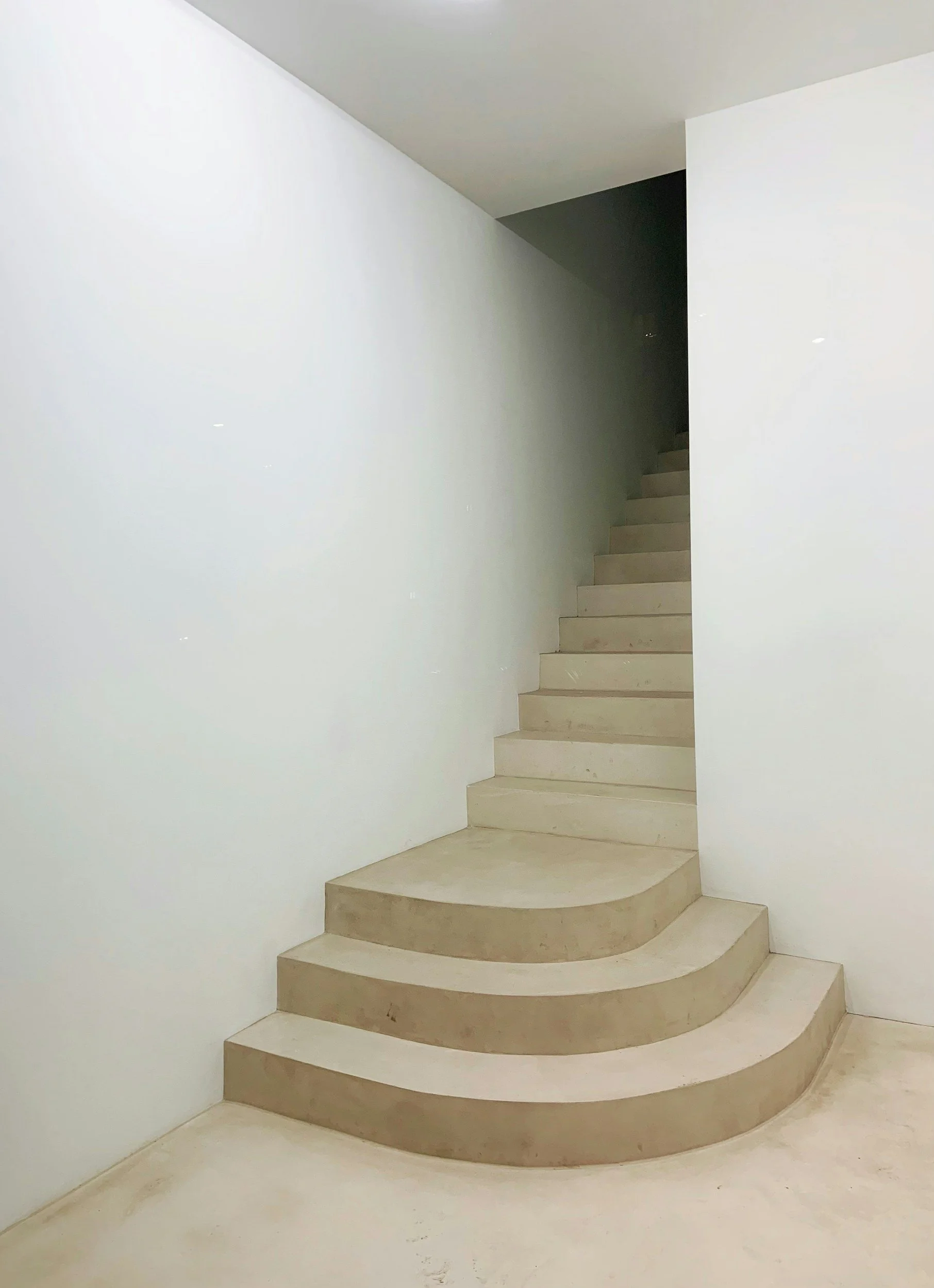Curved beige staircase leading to an upper floor, located between plain white walls.