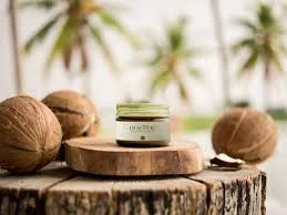 A small jar of skincare or cosmetic cream on a wooden surface with coconuts and a tropical background.