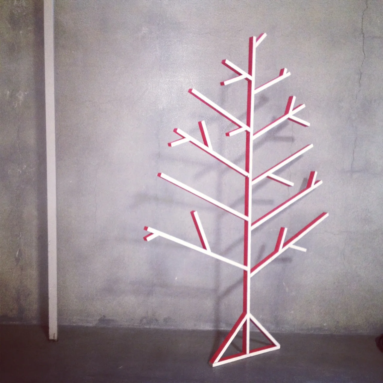 Decorative white and red tree-shaped wall shelf or art piece against a plain wall.