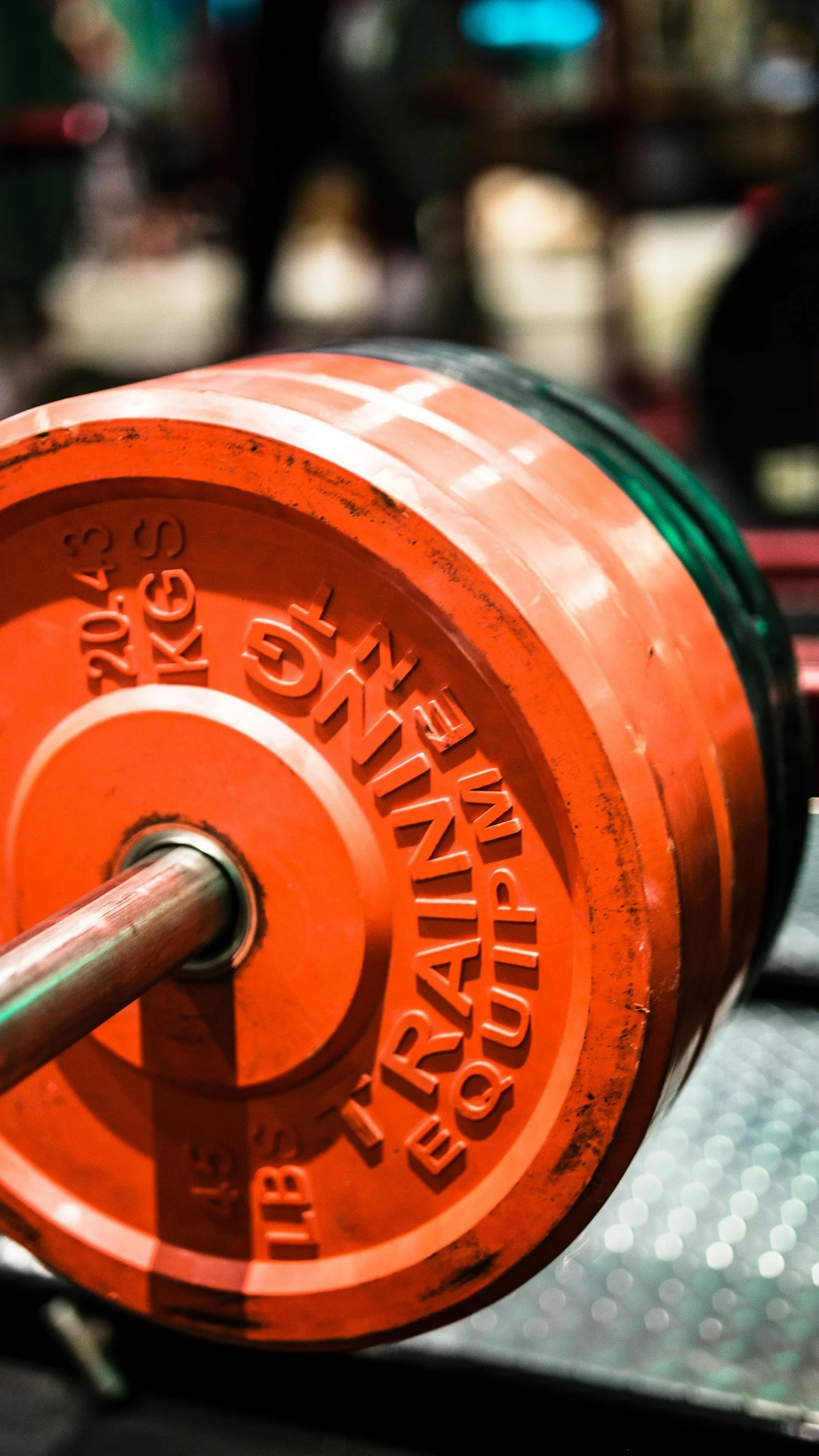 Close-up of an orange rubber weight plate on a barbell in a gym.