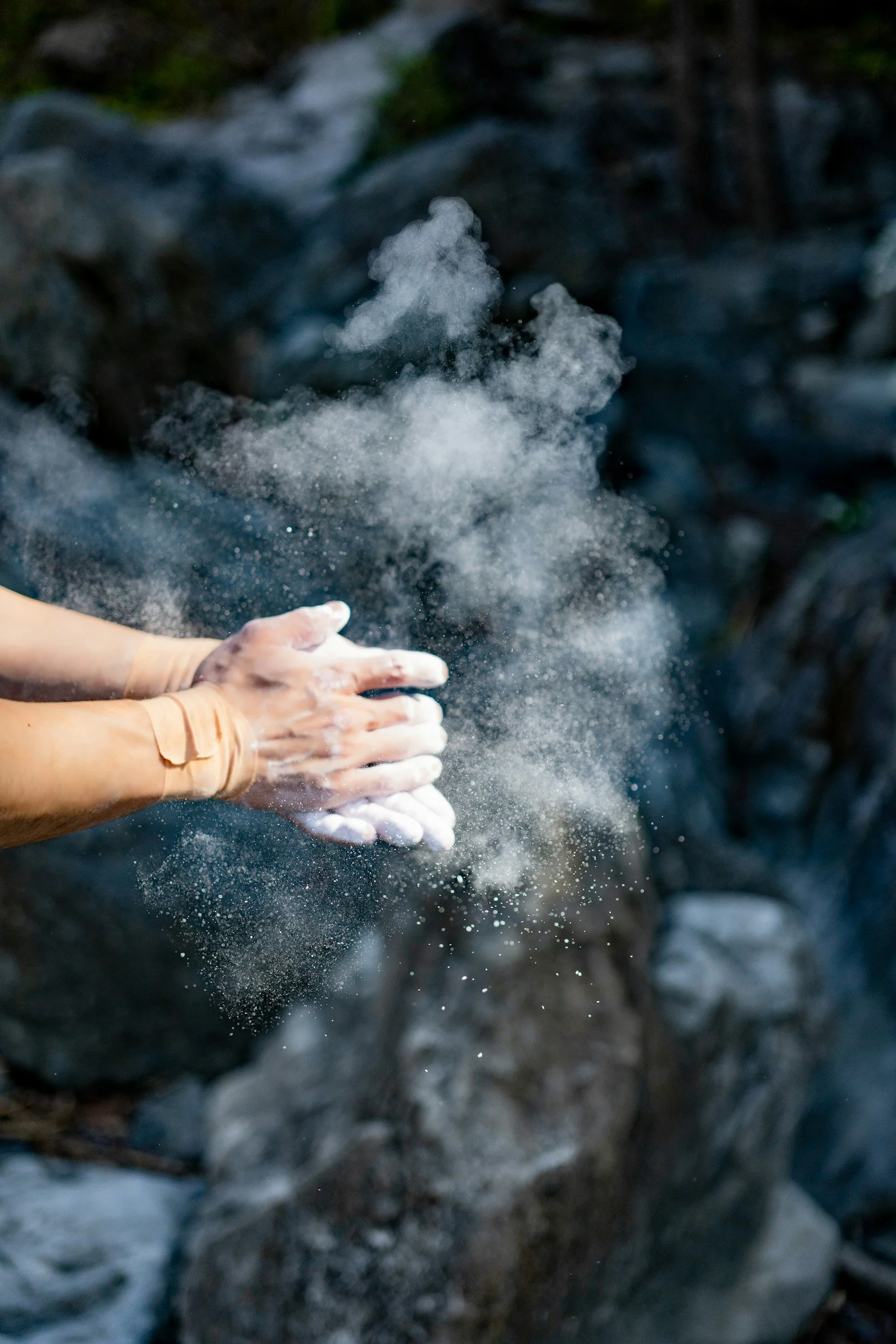 Person washing hands in a stream of cold water outdoors, surrounded by rocks and nature.