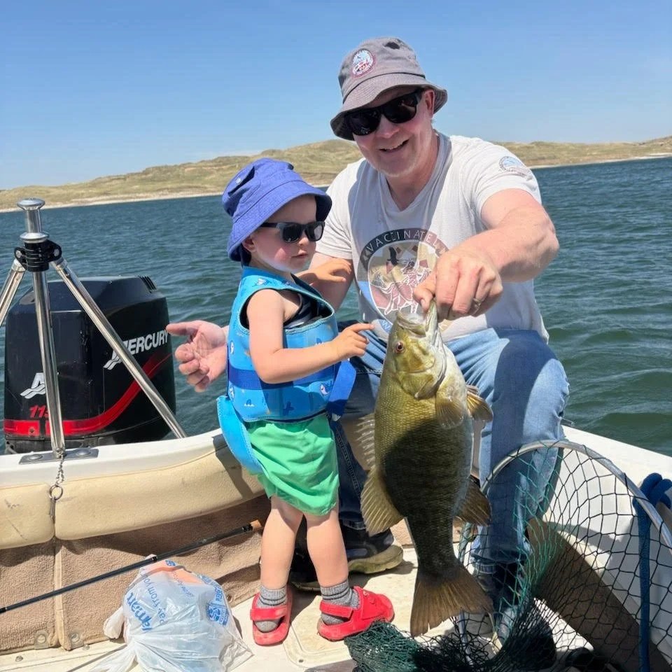 Nick and co. holding a large fish they caught. The background shows water and distant land under a clear blue sky.