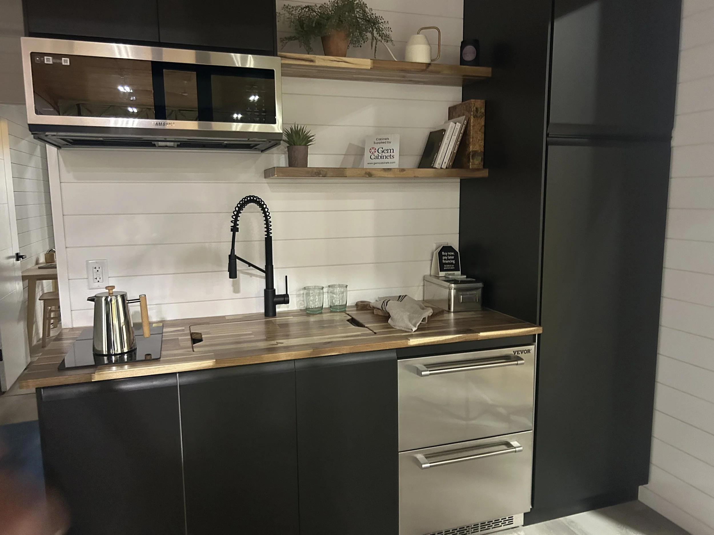 Modern kitchen with black cabinets, wooden countertop, stainless steel appliances, black faucet, and white shiplap wall.