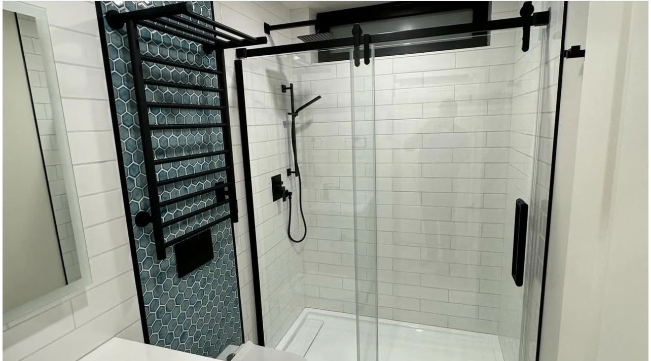Modern walk-in shower with glass doors, white subway tile walls, black fixtures, and a black towel rack.