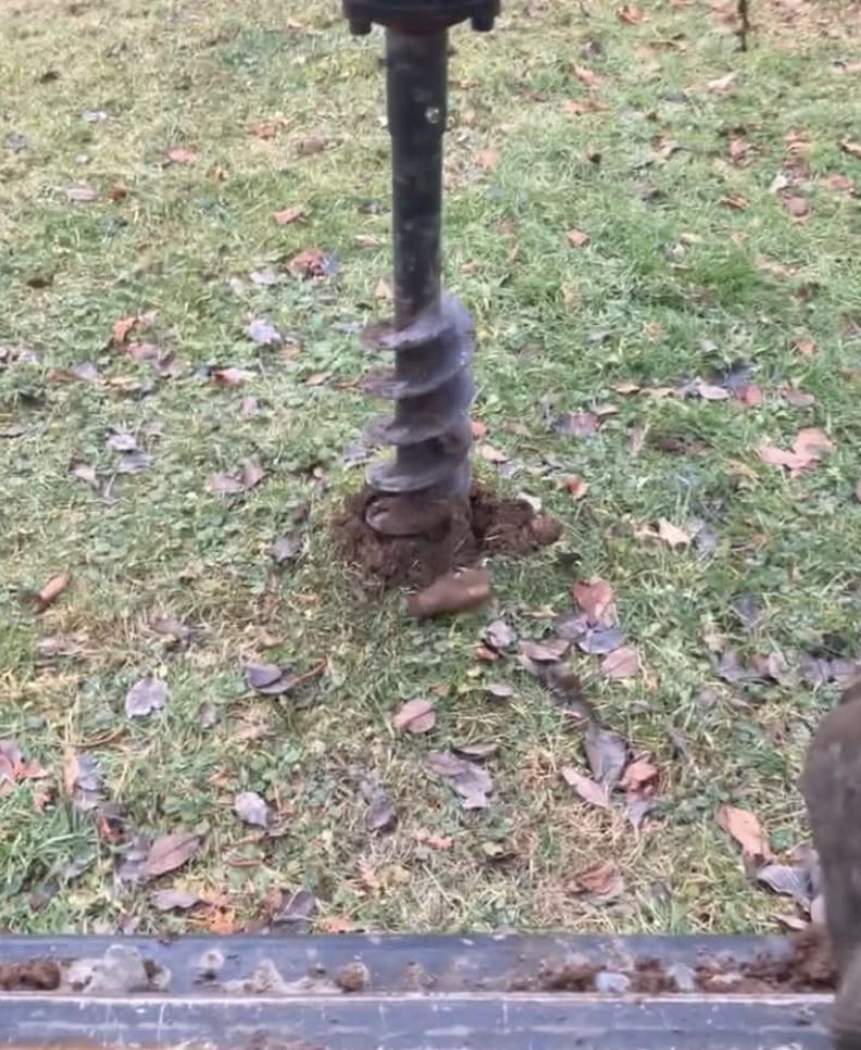 A metal auger bit sticking into the ground with grass and fallen leaves around it.