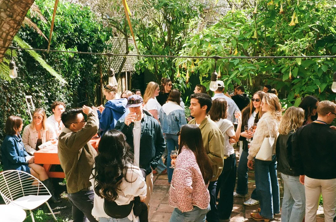 People socializing outdoors in a lush, green garden setting with string lights