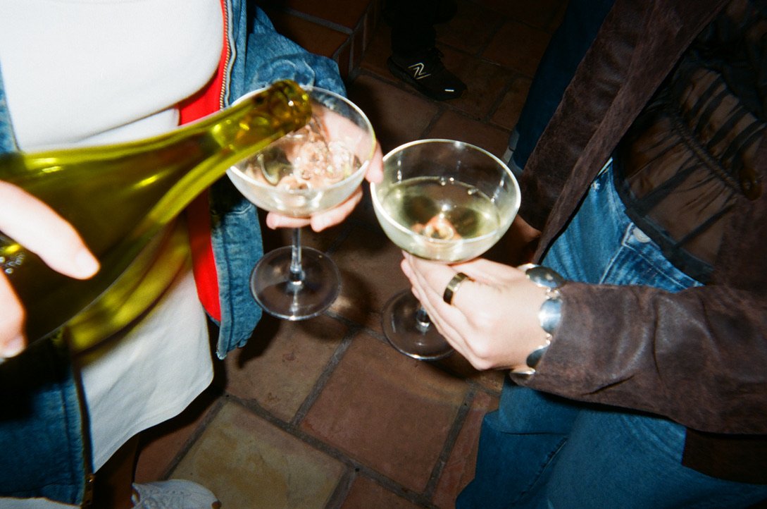 Two people holding glasses of white wine, with one person pouring wine into a glass.