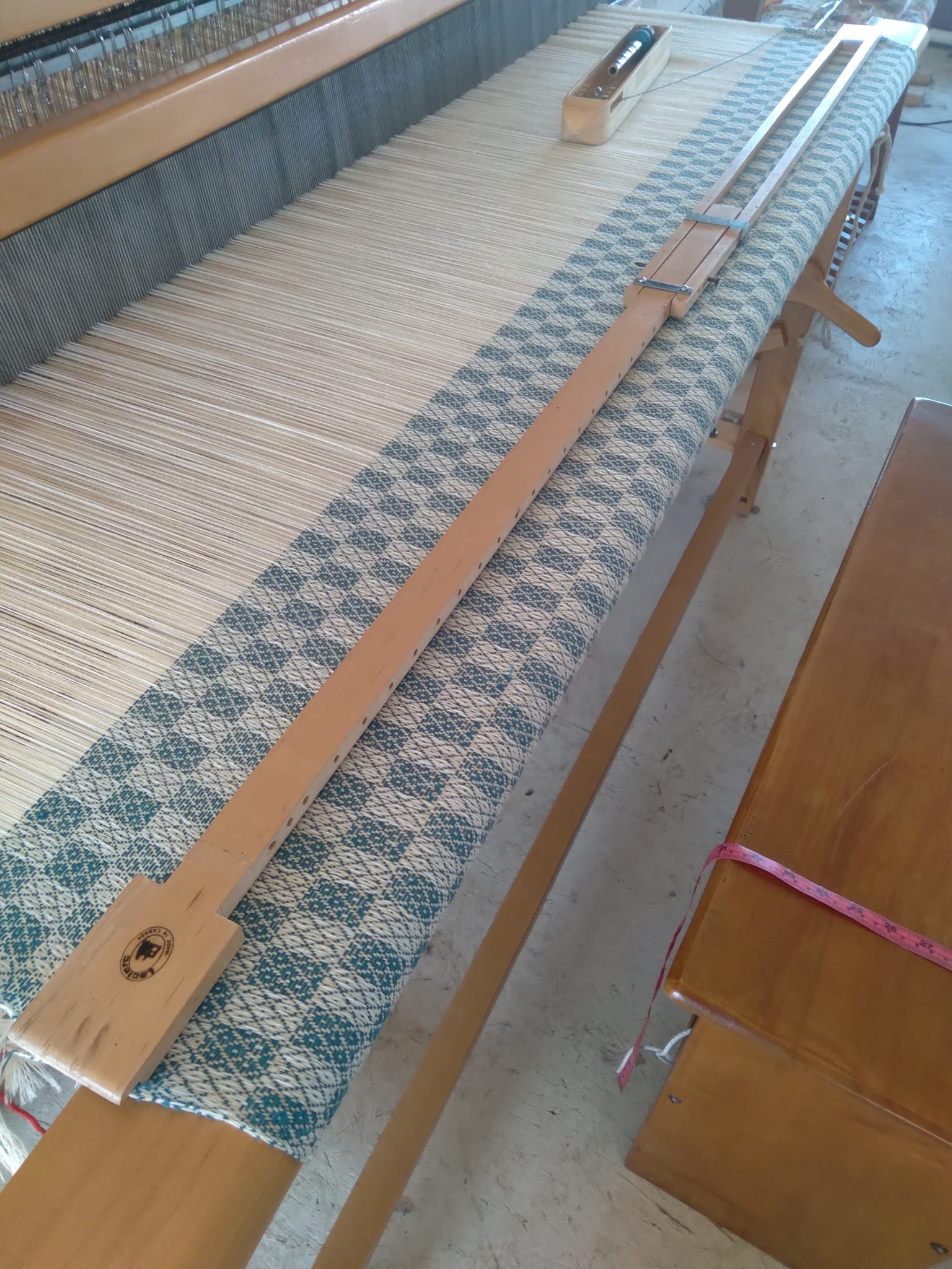A weaving loom with blue and white patterned fabric in progress.