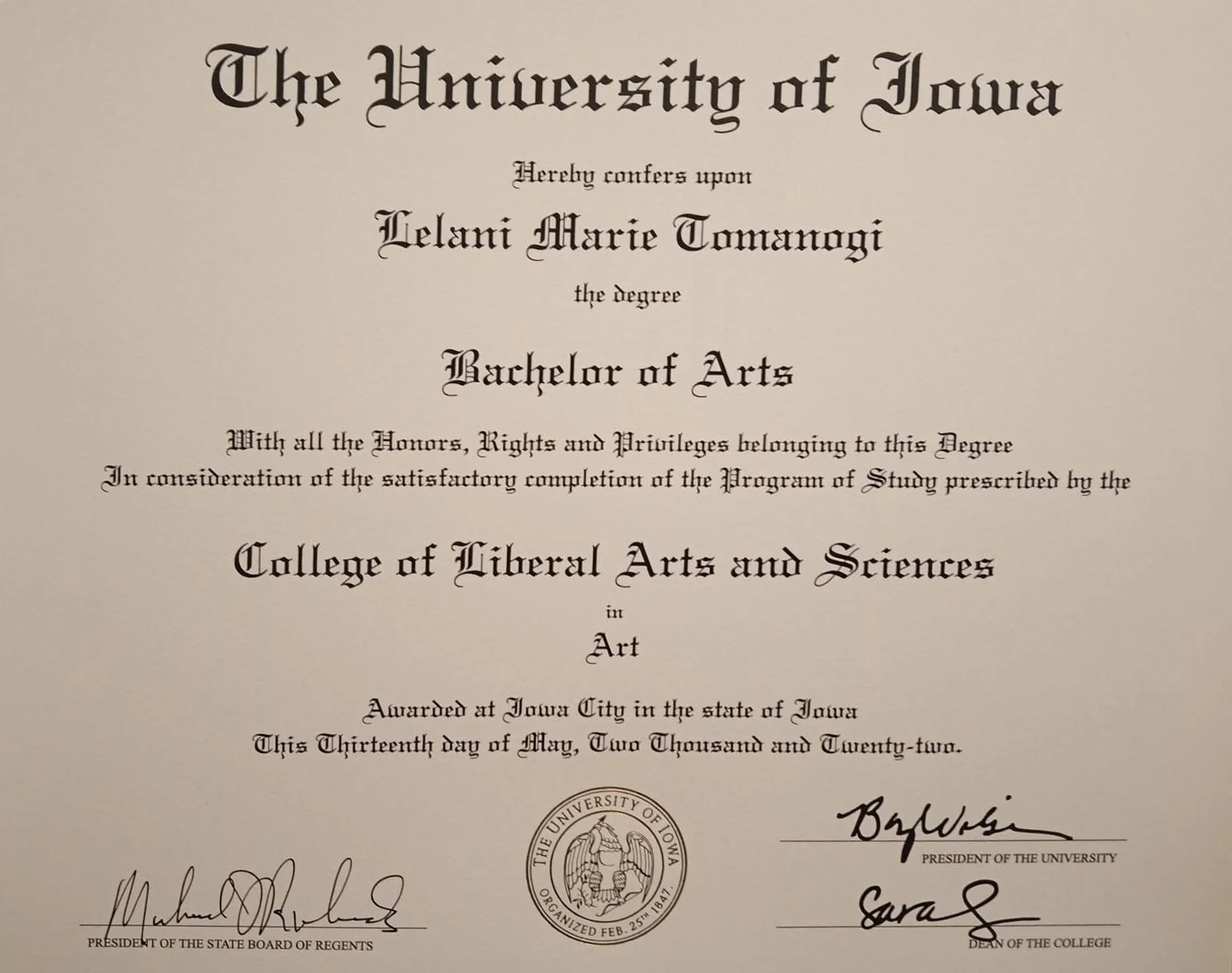 Degree certificate from the University of Iowa awarded to Lelani Marie Tomanogi for a Bachelor of Arts in Art, signed by university officials.