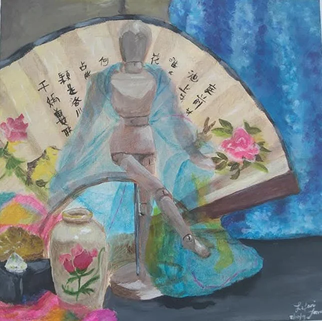 A statue of a woman dressed in traditional Japanese attire holding a pink flower, surrounded by a fan with Chinese characters and pink flowers, a decorative vase with a pink flower, and colorful textiles.