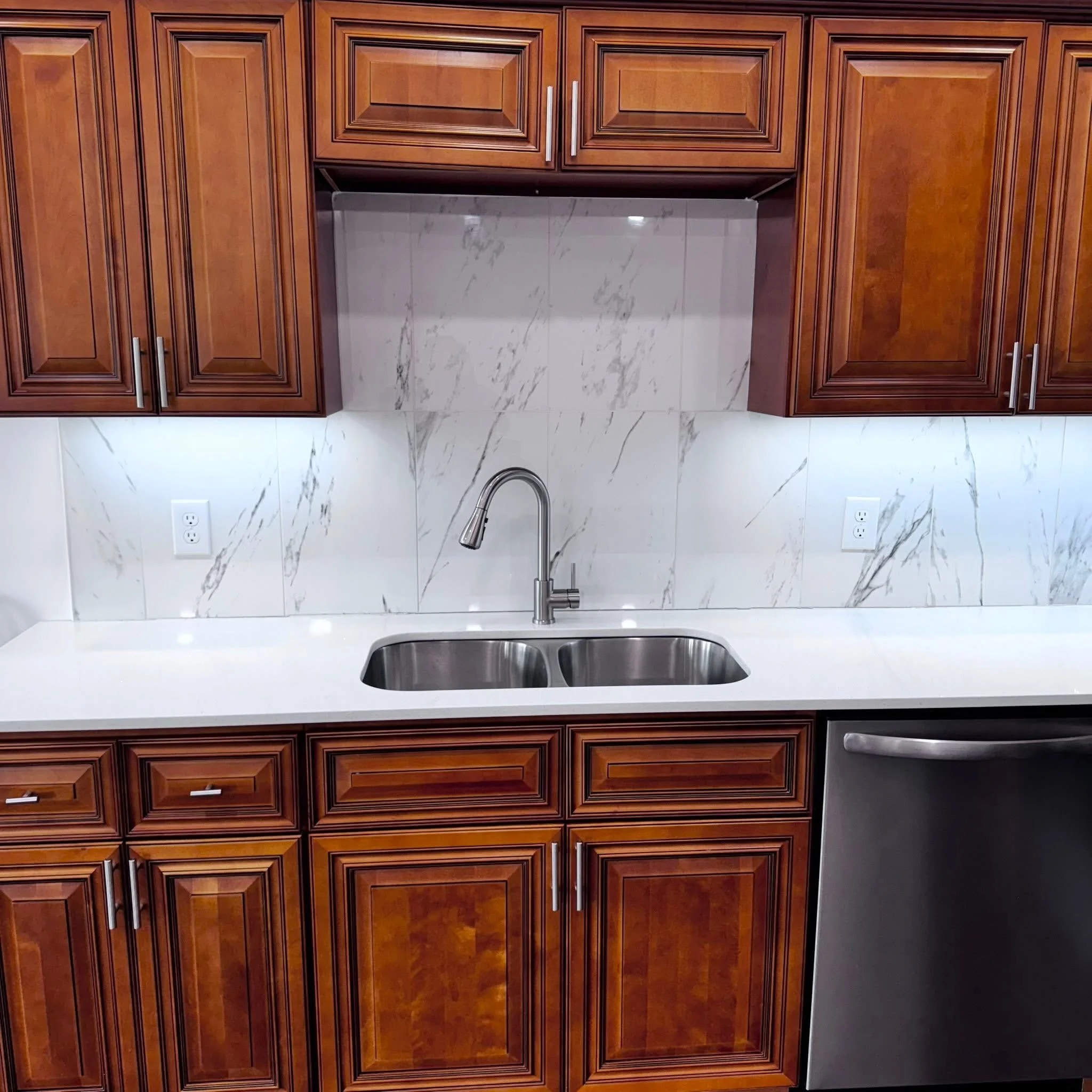 Kitchen with wooden cabinets, a white countertop, a double stainless steel sink, a chrome faucet, a marble backsplash, and a stainless steel dishwasher.