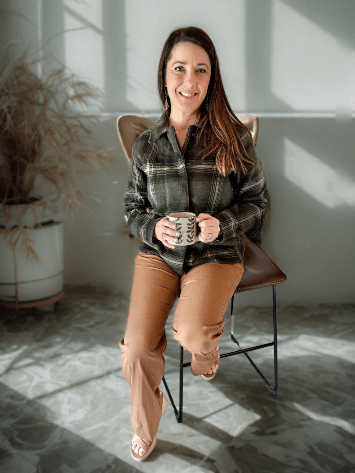 Claire the owner of Cultivate Designs is sitting on a bar stool with a cup of coffee