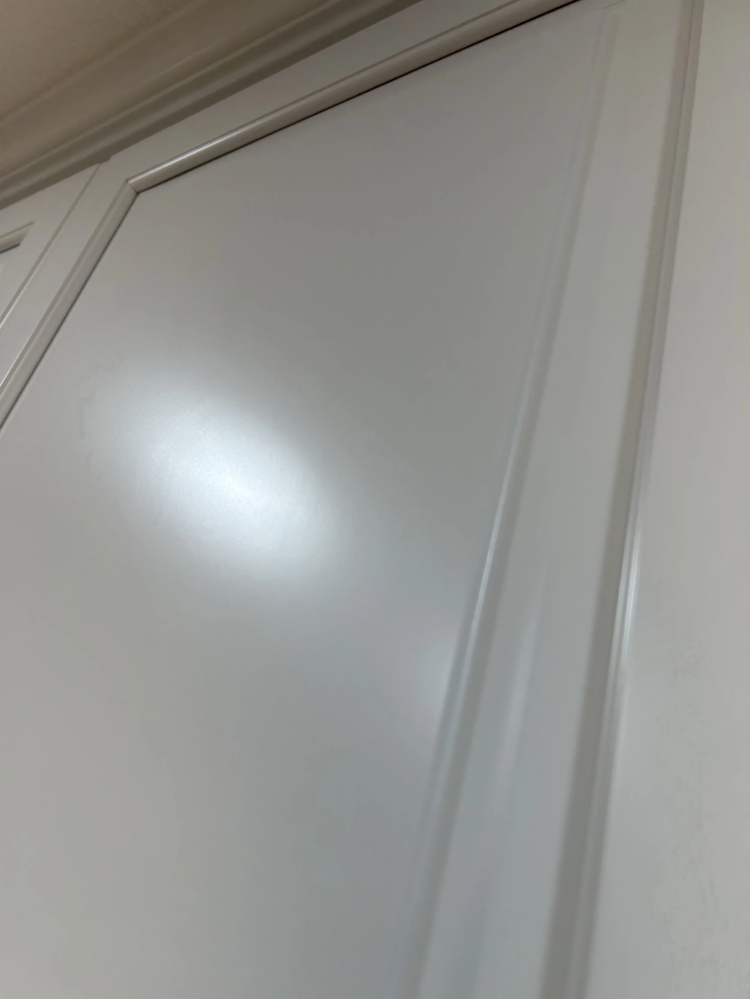Close-up photograph of a white sliding closet door with a glossy finish and decorative trim, slightly open.
