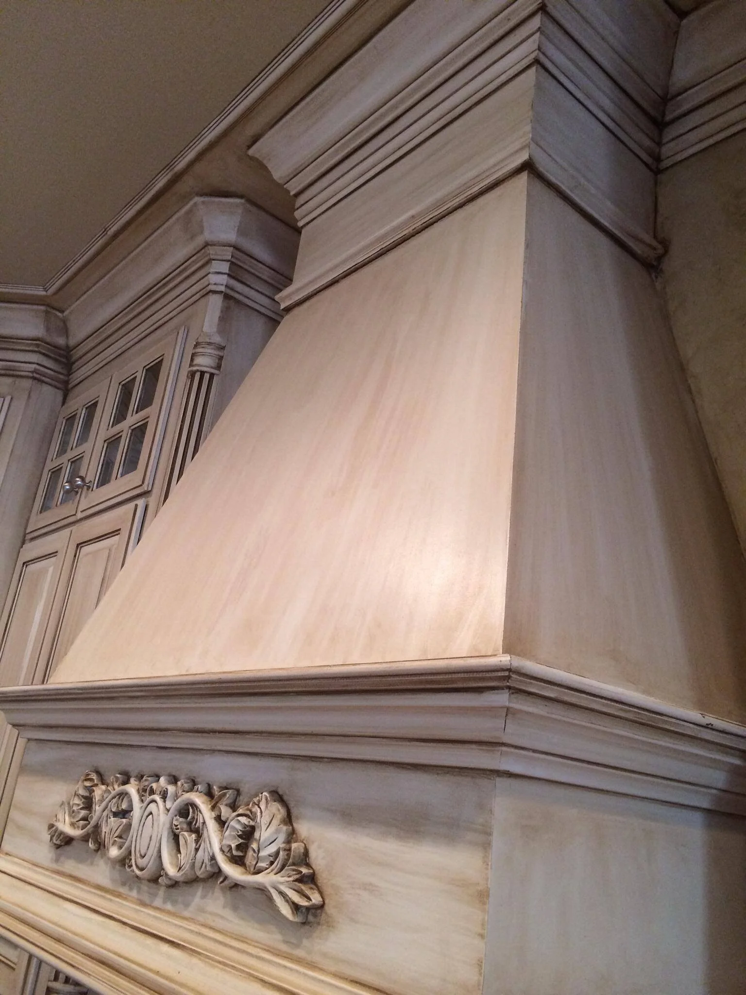 Close-up of a beige-colored kitchen range hood surrounded by cabinetry with decorative molding.