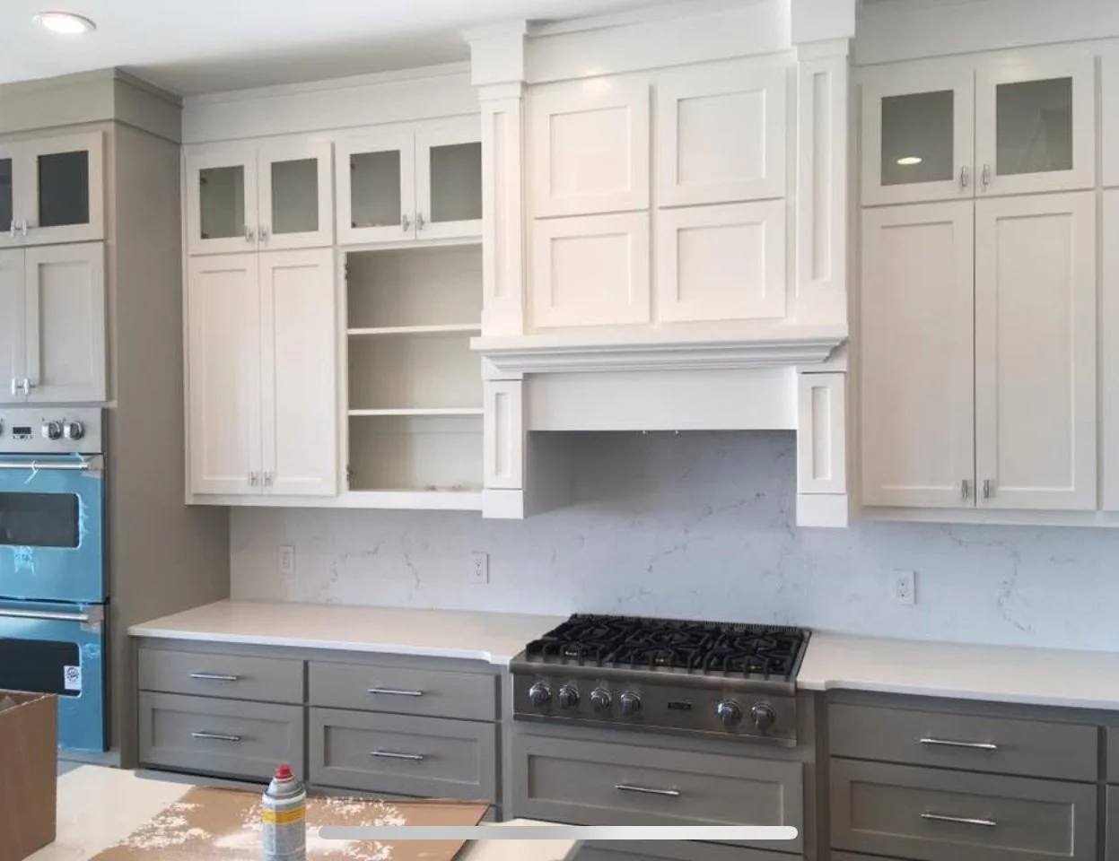 Kitchen with white and gray cabinets, marble backsplash, stainless steel stove, and blue oven on the left.